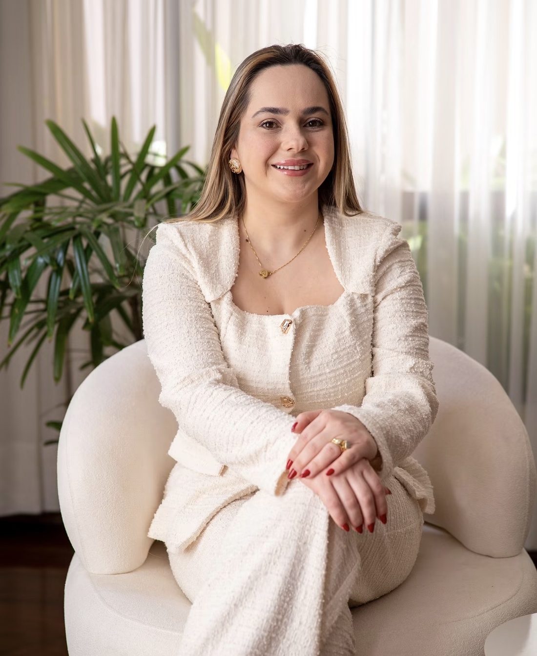 Dra. Lorayne Reche de conjunto marfim, sentada em uma poltrona